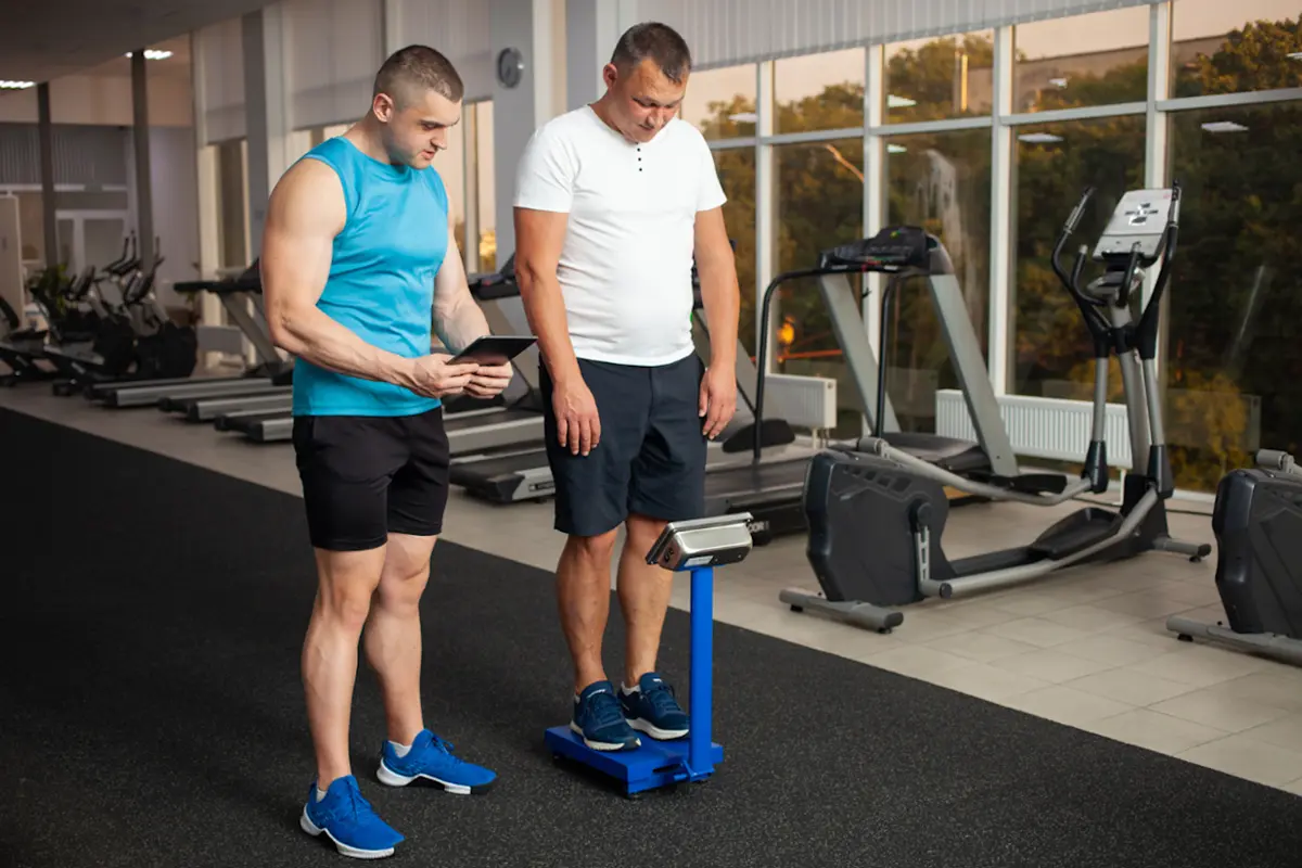 Man in the gym getting weighed by a coach