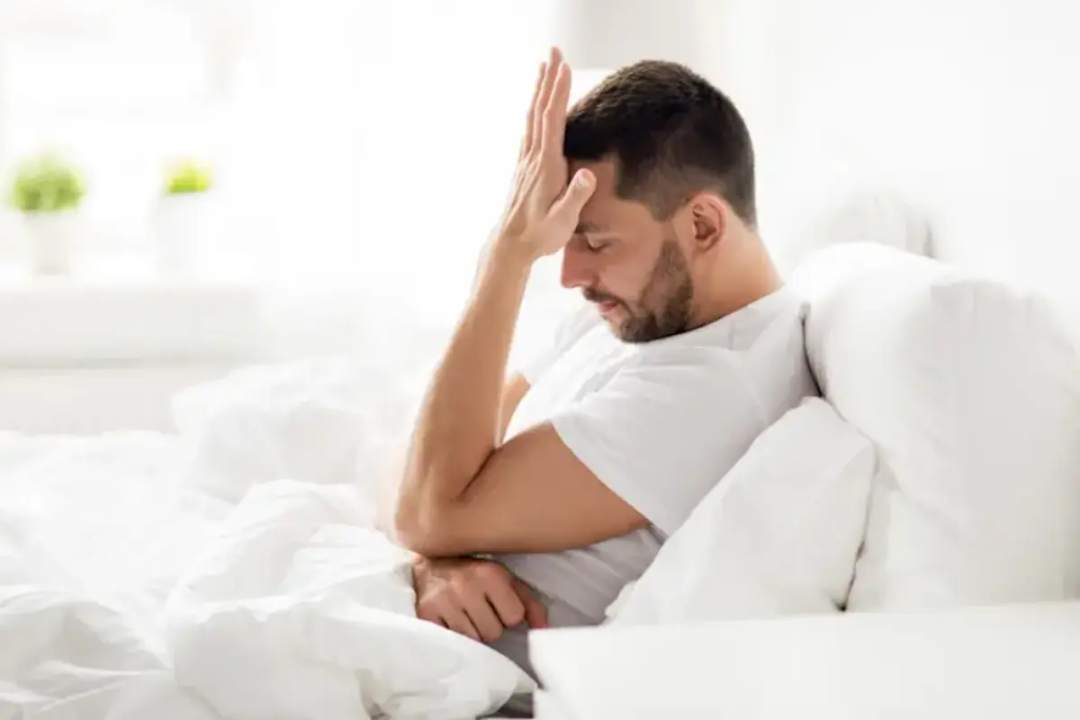 Man sitting up in bed looking tired and uncomfortable